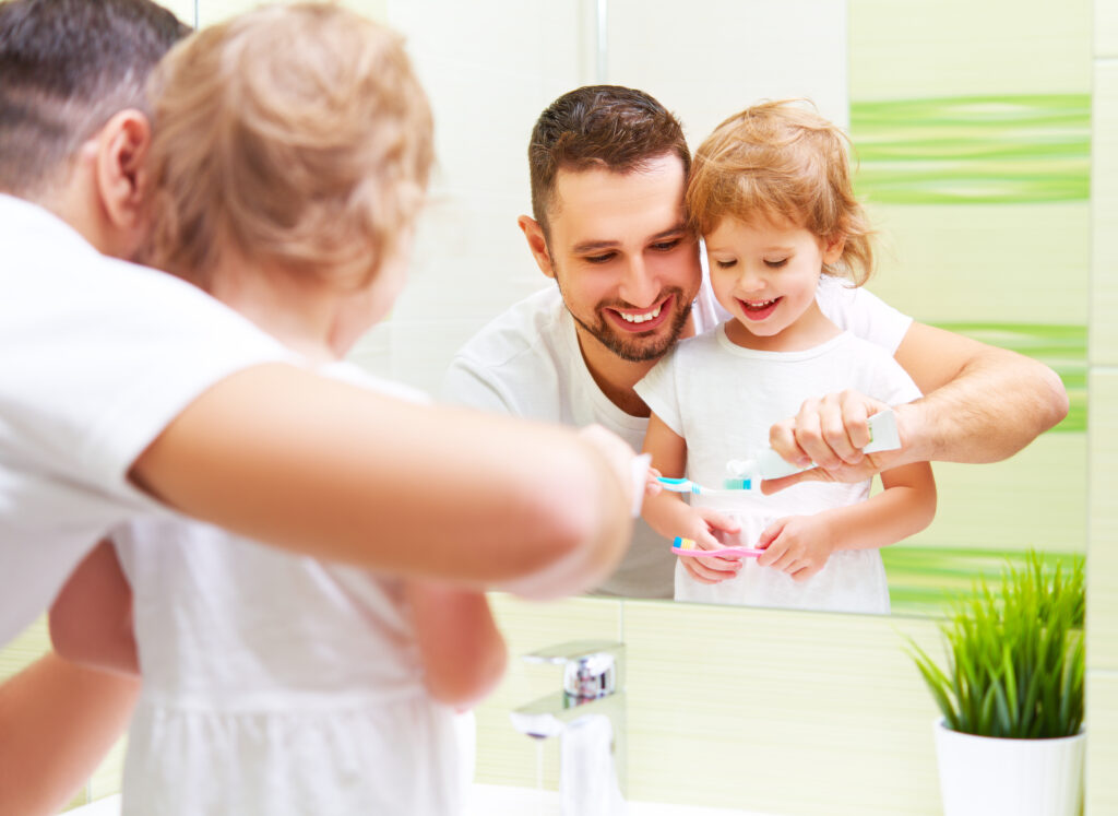 Happy Family Father and Child Girl Brushing Her Teeth In Bathroom